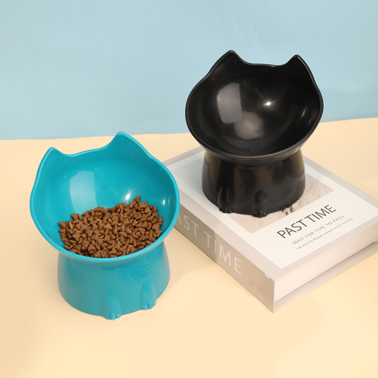 Gamelle pour chat inclinée tête de chat bleue croquettes et noire sur livre - Dîner-Levé™